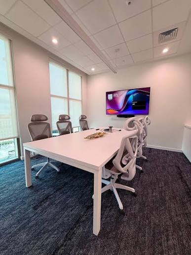Sala de reuniones con mesa blanca, sillas ergonómicas y pantalla